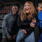 Three people laughing and standing close together in front of a sign that reads "Pendle Witch Trial".