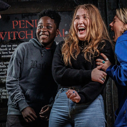 Three people laughing and standing close together in front of a sign that reads "Pendle Witch Trial".