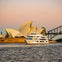 A ferry on the water near the Sydney Opera House and Sydney Harbour Bridge during sunset, with a pastel sky.