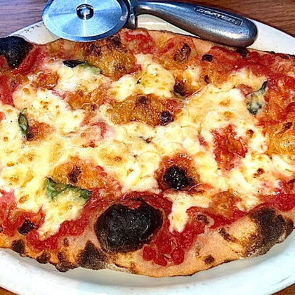 A freshly baked pizza with melted cheese, tomato sauce, and basil on a plate, accompanied by a pizza cutter.