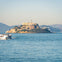 A distant view of Alcatraz Island with its iconic buildings, surrounded by water, and a ferry sailing nearby.