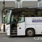 A white coach bus parked on a city street with its front door open and a driver visible inside.