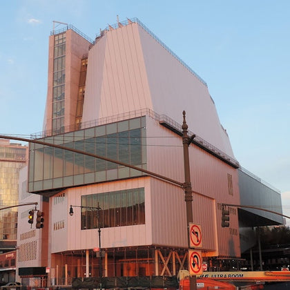Modern building with angular design and large glass windows. Traffic lights and "No Turn" signs visible in the foreground.