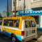 A van with a yellow canopy parked in front of a tour office with a sign that reads "Dylan's Tours."