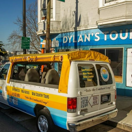 A van with a yellow canopy parked in front of a tour office with a sign that reads "Dylan's Tours."