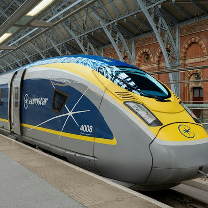 A Eurostar train stopped at a station with an arched glass roof and a brick building in the background.