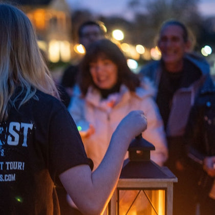 The supplier holds a lantern as guests surround them to listen to ghost stories.