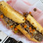 A sandwich filled with shredded meat, diced vegetables, and seasoning on a toasted bun, placed on white parchment paper.