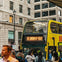 A yellow double-decker bus with "See London by Night" on its display, surrounded by people on a city street.
