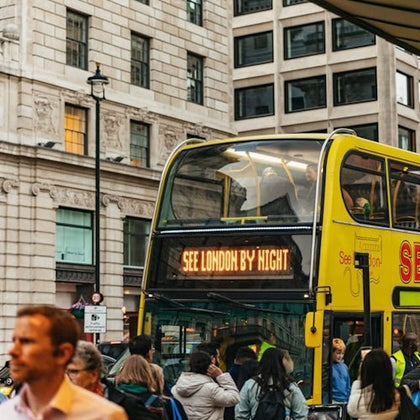 A yellow double-decker bus with "See London by Night" on its display, surrounded by people on a city street.