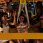 A group of people enjoying a nighttime boat ride, with some raising their hands and smiling, under yellow lighting.