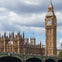 The Palace of Westminster and Big Ben with a crowded bridge in the foreground under a partly cloudy sky.