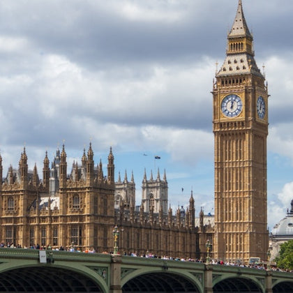 The Palace of Westminster and Big Ben with a crowded bridge in the foreground under a partly cloudy sky.