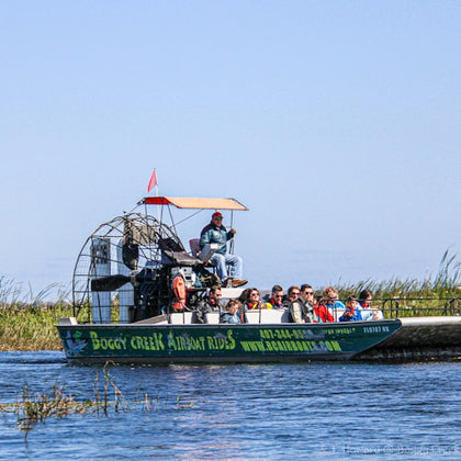 Tourists seated on an airboat in a marshland, with a captain at the helm and tall grasses in the background.