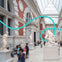 People walking and sitting near classical statues in a spacious, skylit museum hall with a modern blue sculpture overhead.