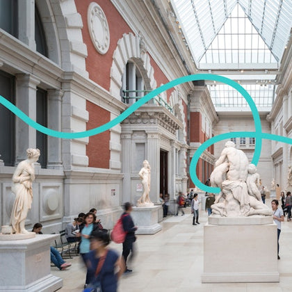 People walking and sitting near classical statues in a spacious, skylit museum hall with a modern blue sculpture overhead.