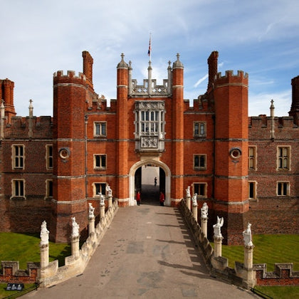 A large, historic brick building with towers and statues on either side of the entrance under a blue sky. A flag flies at the top.