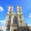 A large Gothic cathedral with two tall towers, intricate architectural details, and a clock on the left tower, set against a blue sky.