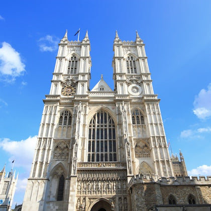A large Gothic cathedral with two tall towers, intricate architectural details, and a clock on the left tower, set against a blue sky.