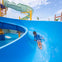 A child sliding down a blue water slide in a water park under a clear sky.