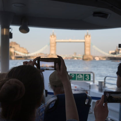People on a boat taking photos of Tower Bridge in London during daylight.
