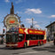 A red double-decker tour bus labeled "BIG BUS SAN FRANCISCO" passes by a large Fisherman's Wharf sign under a clear blue sky.