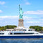 The Statue of Liberty with a NY Waterway ferry passing in the foreground on a sunny day.