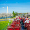 Tourists on an open-top bus viewing the Washington Monument and blooming cherry trees under a clear blue sky.