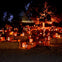 A nighttime Halloween scene with numerous carved, lit pumpkins on hay bales, and faintly visible people among them.