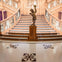 A grand wooden staircase with ornate railings and a statue holding a lamp on a pedestal at the base.