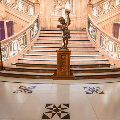 A grand wooden staircase with ornate railings and a statue holding a lamp on a pedestal at the base.