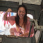 A person smiling and posing while climbing through a hatch of a metal structure, with others visible in the background.