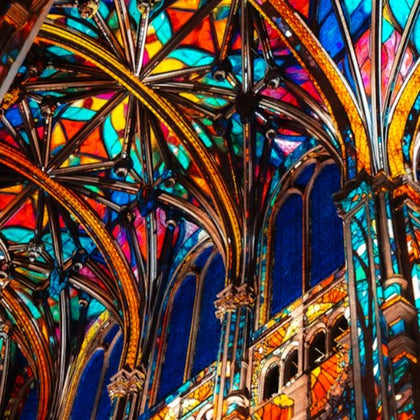 Intricate stained glass windows and colorful arched ceilings of a Gothic-style cathedral.