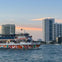 A colorful boat named "Miss Miami" on water with tall buildings and a sunset sky in the background.
