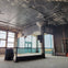 A large, industrial-style room with peeling paint, large windows, a column, and a metal railing across the floor.