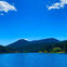 A serene lake with people on paddleboards, surrounded by forested hills under a blue sky with a few clouds.