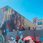 A mural featuring a detailed portrait on a building wall, with graffiti below and a red Wilson umbrella in the foreground.