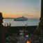 A white ferry with passengers floats on a calm sea at sunset, seen through a window from a dining table.