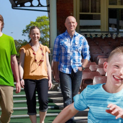 A group of four people outdoors, with three walking and one running in the foreground, near a building and seating area.
