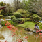 A serene garden scene with a pond, greenery, and a person and child by the water's edge on a rock platform.