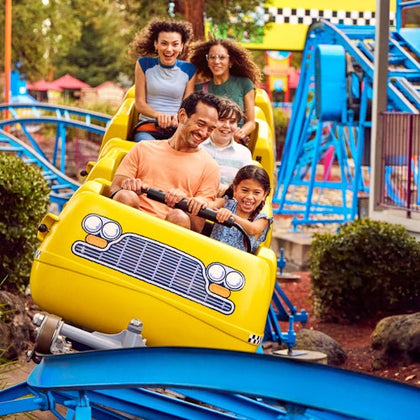 A group of people enjoying a ride on a small roller coaster with bright yellow car-shaped cars.