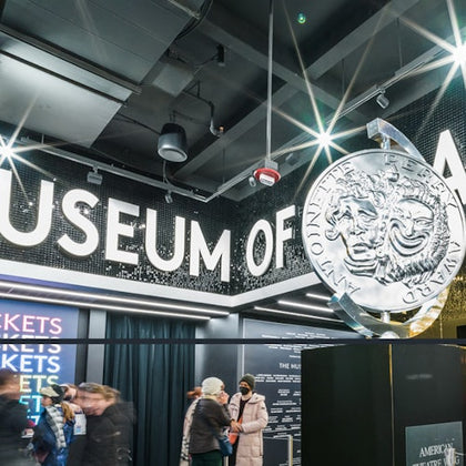 People in a museum lobby with a large coin sculpture and "Museum of" signage visible.