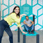 Two people at the Museum of Illusions in New York, interacting with an oversized chair exhibit creating a visual illusion.