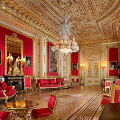 An ornate room with red and gold decor, elegant furniture, large chandeliers, and detailed wall and ceiling patterns.