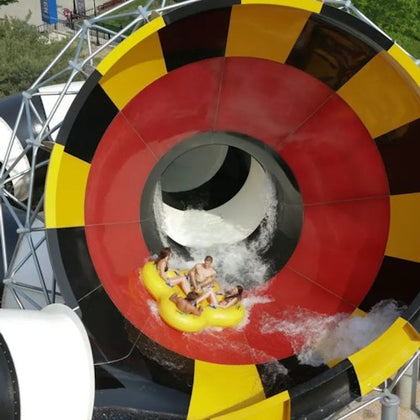 Four people on a yellow inflatable raft exiting a colorful water slide with red, yellow, and black patterns.