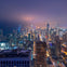 Aerial view of a city skyline at night with illuminated skyscrapers and buildings under a hazy purple sky.