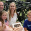 A group of people sitting outdoors near bicycles, with a young girl holding an American flag and others smiling at the camera.