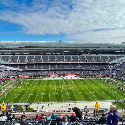 Football stadium with players warming up on the field and spectators in the stands under a partly cloudy sky.