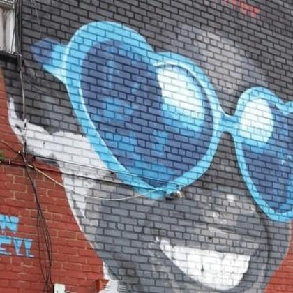 A mural painted on a brick wall depicting a smiling face wearing large, blue, heart-shaped sunglasses.