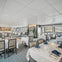 A modern dining room with neatly set tables, white tablecloths, and blue napkins, located in a bright and spacious area.